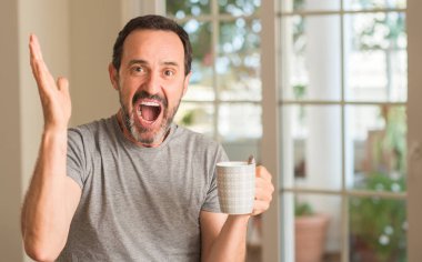 Kocaman bir gülümseme ile çığlık zaferini kutluyor ve ellerini kaldırdı bir fincan çok mutlu ve heyecanlı, kazanan ifadesinde kahve içme orta yaş erkek