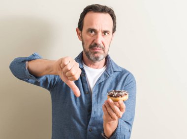 Kızgın yüz ile üst düzey adam yeme çikolata çörek, başparmak aşağı, ret kavramı ile eksi işareti gösterilen sevmemek