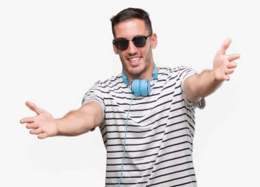 Yakışıklı genç giyen kulaklık sarılmak için kollarını açarak gülümseyerek kameraya bakarak adam. Neşeli ifade kucaklayan mutluluk.