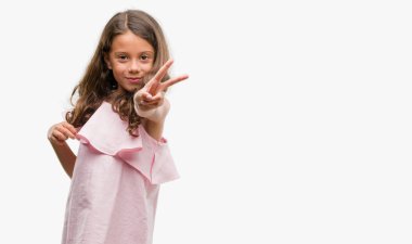 Zafer işareti yapıyor parmak gösterilen kameraya bakarak gülen esmer Latin kız giyiyor pembe elbise. İki numaralı.