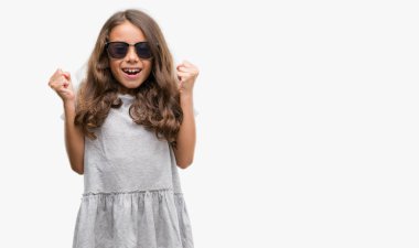 Esmer Latin kız kutluyor güneş gözlüğü takıyor şaşırttı ve silah ile başarı için yükseltilmiş ve açık gözler hayrete düşürdü. Kazanan kavramı.