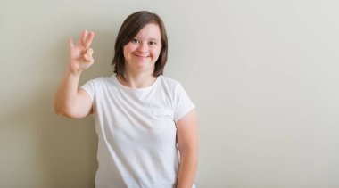 Gösterilen ve parmakları ile işaret duvar üzerinde duran down sendromu kadın kendinden emin ve mutlu gülümseyerek iken üçüncü.