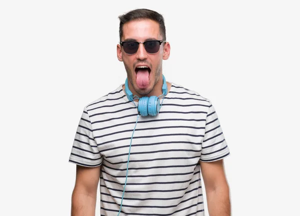 Όμορφος Νεαρός Άνδρας Φορώντας Ακουστικά Κολλήσει Γλώσσα Έξω Χαρούμενος Αστεία — Φωτογραφία Αρχείου