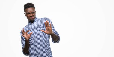 Young african american man wearing blue shirt disgusted expression, displeased and fearful doing disgust face because aversion reaction. With hands raised. Annoying concept. clipart