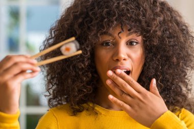 Afrikalı-Amerikalı kadın kapak ağız el ile şok chopsticks evde için hata, ifade korku, utanç ile kullanarak suşi yemek sessizlik içinde gizli kavramı korkuttu