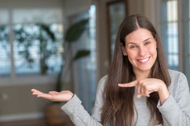 Genç güzel kadın evde şaşırdım ve el ile sunulması ve parmak ile işaret ederken kameraya gülümseyen.