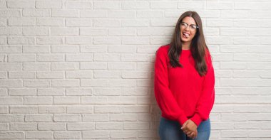 Dil yapışkanlık dışarı beyaz tuğla duvarın üzerinden komik bir ifadeyle mutlu duran genç esmer kadın. Duygu kavramı.