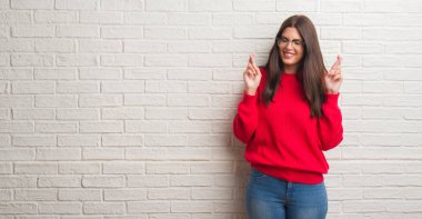 Umut ve gözleri kapalı geçiş parmaklarıyla gülümseyen beyaz tuğla duvarın üzerinden duran genç esmer kadın. Şans ve batıl kavramı.