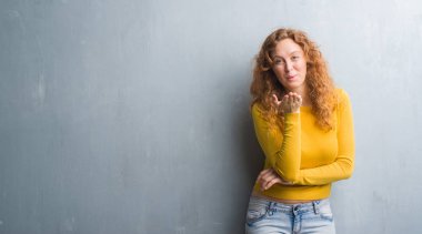 Bir öpücük el ile güzel ve seksi olmak hava üfleme kamera bakarak gri grunge duvarın üzerinden genç Kızıl saçlı kadın. Aşk ifade.
