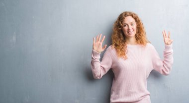 Gri grunge genç Kızıl saçlı kadın duvar gösterilen giymiş pembe kazak ve parmakları ile işaret gülümseyen ise kendinden emin ve mutlu 8 numaralı.