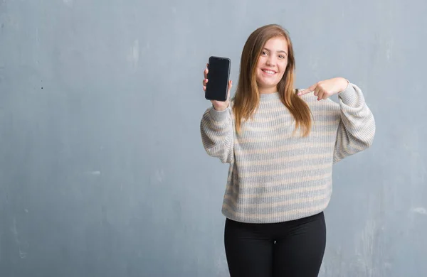 Молодая Взрослая Женщина Серой Гранж Стене Показывает Чистый Экран Смартфона — стоковое фото