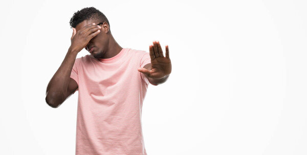 Young african american man wearing pink t-shirt covering eyes with hands and doing stop gesture with sad and fear expression. Embarrassed and negative concept.