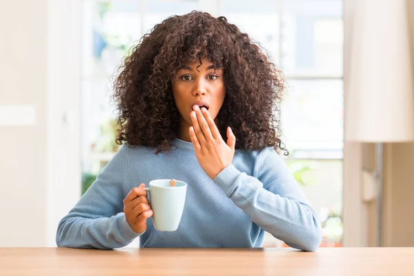 非洲裔美国妇女拿着一杯咖啡在家里捂住嘴用手震惊的错误 表达恐惧 害怕沉默 秘密概念 — 图库照片