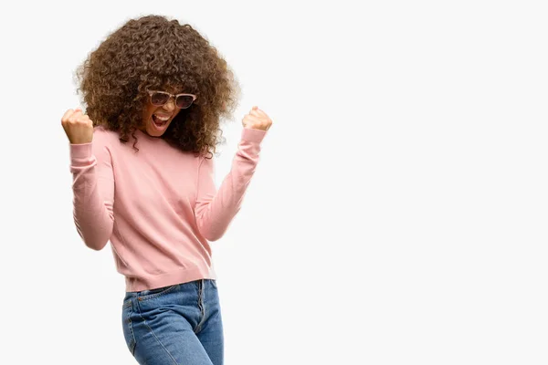 アフリカ系アメリカ人女性ピンク サングラス非常に幸せと興奮して両手を上げると 勝者のジェスチャーをして笑みを浮かべて 成功のために叫んで お祝いのコンセプト — ストック写真