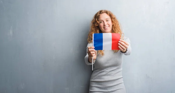 Молодая Рыжая Женщина Над Серой Гранж Стеной Держит Флаг Франции — стоковое фото