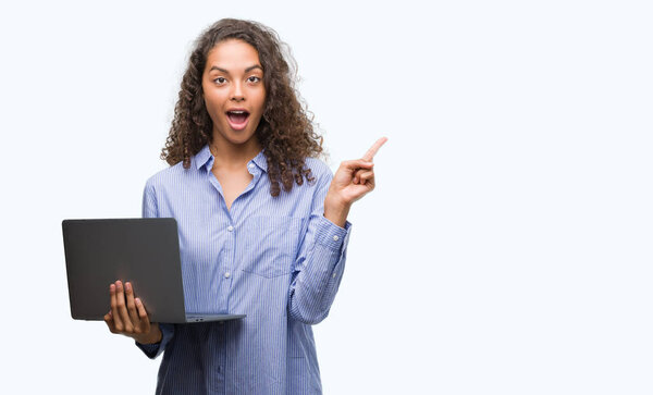 Young hispanic woman holding computer laptop very happy pointing with hand and finger to the side