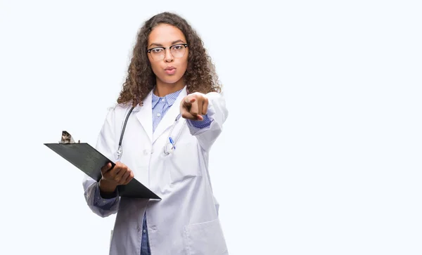 年轻的西班牙裔医生的女人拿着一个剪贴板指向相机和你 正面和自信的手势从前面 — 图库照片