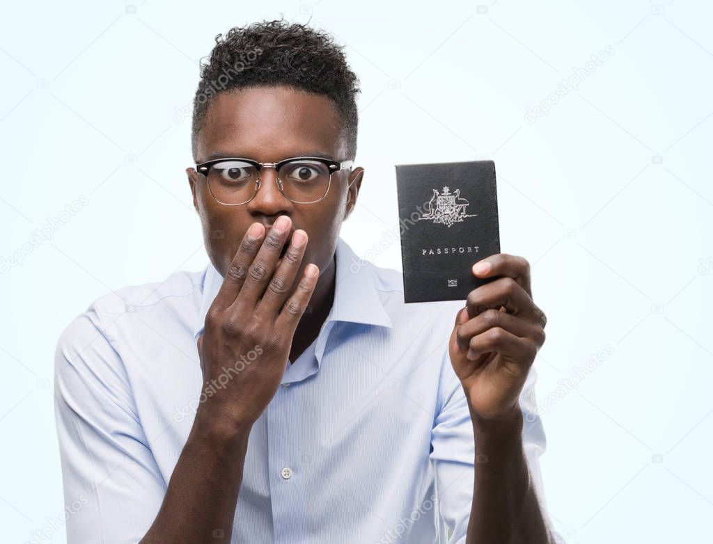 Young african american man holding australian passport cover mouth with hand shocked with shame for mistake, expression of fear, scared in silence, secret concept
