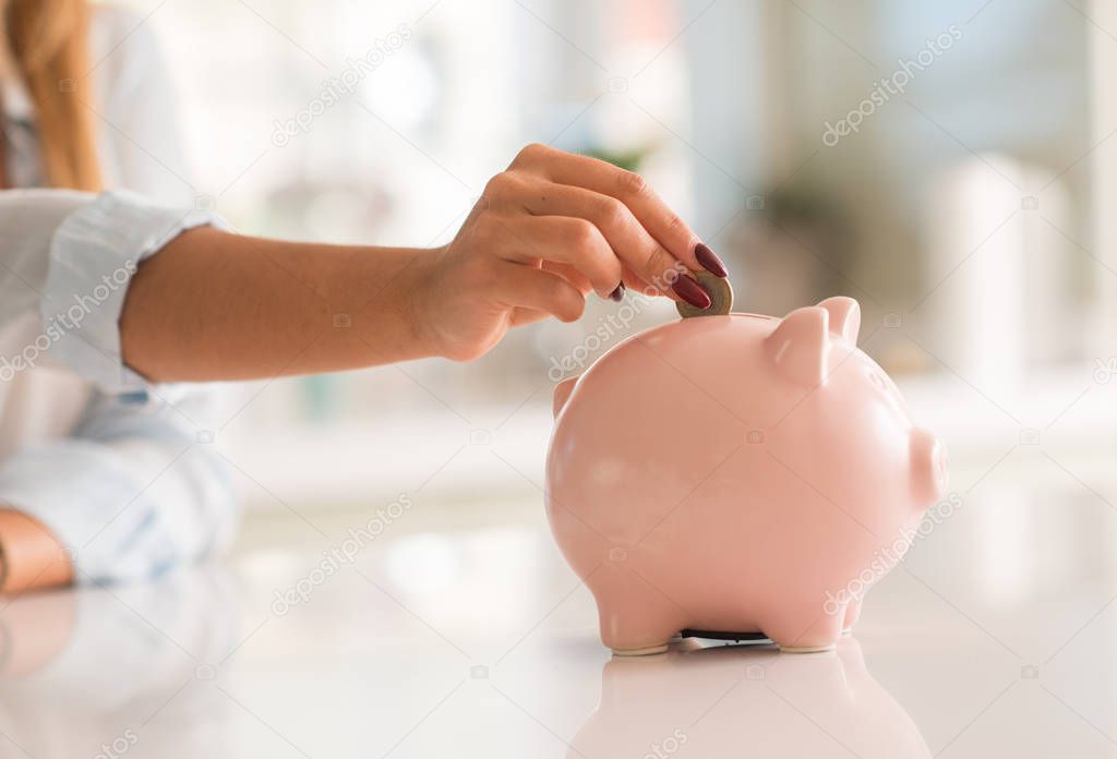 Beautiful young woman hands holding a coin investing in to a piggy bank at home. Business concept.