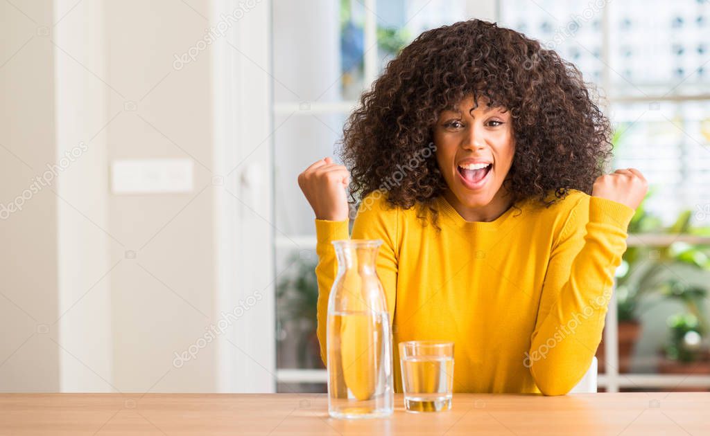 African american woman drinking a glass of water at home screaming proud and celebrating victory and success very excited, cheering emotion