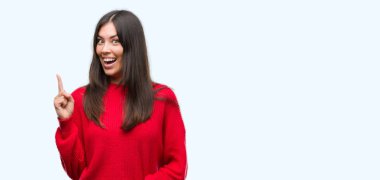 Kırmızı kazaklı işaret parmağı ile başarılı fikir giyen genç güzel İspanyol. Çıktıktan ve mutlu. Bir numara.