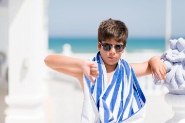 Kızgın yüz, sahilde bir donanma havlu giyen tatil günlerinde genç çocuk negatif antipati başparmak aşağı, ret kavramı ile gösterilen işareti