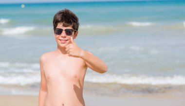 Sahilde büyük gülümseme ok işareti, başparmak ile parmak, mükemmel işareti yapıyor ile mutlu tatil günlerinde genç çocuk