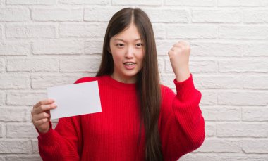 Tuğla Genç Çinli kadın boş kağıt rahatsız tutarak ve öfke, deli ile sinirli bağırarak duvar ve yükseltilmiş el ile bağırmaya kavramı öfke