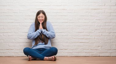 Tuğla duvar ellerle birlikte AF emin gülümseyen için soran dua üzerinde katta oturan genç Çinli kadın.