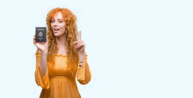 Genç Kızıl saçlı kadın holding pasaport Amerika Birleşik Devletleri bir fikir ya da soru işaret parmağı gülen yüz, bir numara ile şaşırttı