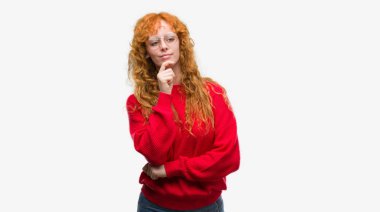 Emin çapraz kollar ve çeneme kaldırdı el ile gülümseme ile kameraya bakarak kırmızı kazak giyen genç Kızıl saçlı kadın. Pozitif düşünce.