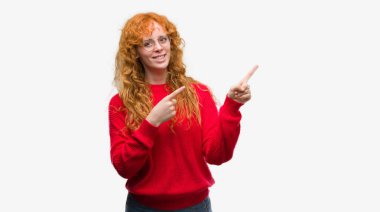 Genç redhead giyen kırmızı kazaklı gülümseyen kadın ve iki elleri ve parmakları ile tarafına işaret kamera bakıyor.
