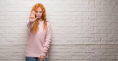 Elin avuç durağı şarkı yapıyor tuğla duvarın üzerinden duran genç Kızıl saçlı kadın. Negatif ve ciddi bir jest yüz ifadesiyle uyarı.