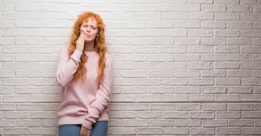 Diş ağrısı veya dişlerde dişlerle ilgili hastalık nedeniyle ağız acı ifadesi ile el ile dokunmak tuğla duvarın üzerinden duran genç Kızıl saçlı kadın. Diş hekimi kavramı.