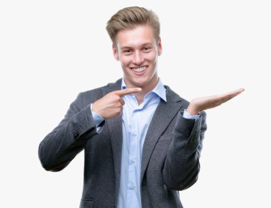 Hayret ve el ile sunulması ve parmak ile işaret ederken kameraya gülümseyen genç yakışıklı sarışın iş adamı.