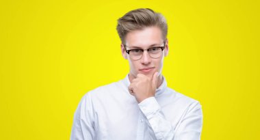 Genç yakışıklı sarışın adam emin çapraz kollar ve çeneme kaldırdı el ile gülümseme ile kameraya bakıyor. Pozitif düşünce.