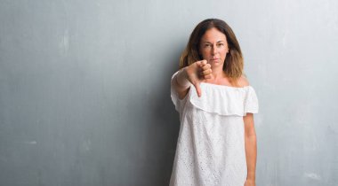 Mutsuz ve kızgın ret gösterilen ve başparmak aşağı hareketi ile negatif seyir gri grunge duvarın üzerinden duran orta yaş İspanyol kadın. Kötü ifade.