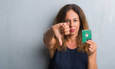 Kızgın yüz, eksi işareti aşağı antipati başparmak ile gösterilen, ret kavramı ile sabit disk tutarak gri grunge duvarın üzerinden duran orta yaş İspanyol kadın