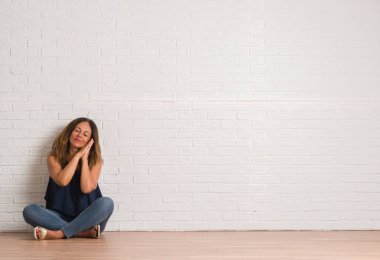 Orta yaş İspanyol kadın yorgun hayal ve eller ile birlikte kapalı gözlerle gülümseyerek poz uyku beyaz tuğla duvarın üzerinden katta oturan.