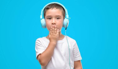 Koyu saçlı küçük çocuk kulaklık kapak ağızlı el ile müzik dinlemek için hata, korku, sessizlik içinde gizli kavramı korkmuş ifade utanç ile şok
