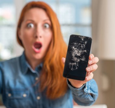 Kırık smartphone bir sürpriz yüz, korkuyor ve heyecanlı korku ifadesi ile şok korkmuş tutan Kızıl saçlı kadın