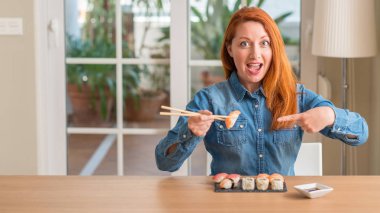 El ve parmak ile işaret çok mutlu yemek çubukları kullanarak suşi yemek Kızıl saçlı kadın