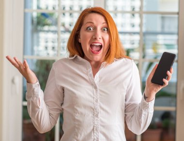 Evde çok mutlu ve heyecanlı, akıllı telefon kullanan Kızıl saçlı kadın kazanan ifade büyük gülümseme ile çığlık ve ellerini kaldırdı zaferini kutluyor
