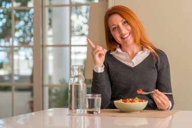 Kızıl saçlı kadın yeme meyve tabağı, kivi ve çilek, çok mutlu el ve parmak ile işaret tarafına Anasayfa