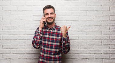 İşaret ve başparmak kadar mutlu yüz gülümseyen tarafı ile gösterilen beyaz tuğla duvarın üzerinden telefon ayakta konuşan genç yetişkin adam