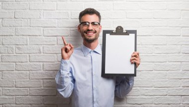 Genç Yetişkin iş adamı tuğla üzerinde tutarak Pano bir fikirle sürpriz duvar veya gülen yüz, bir numara ile işaret parmağı soru