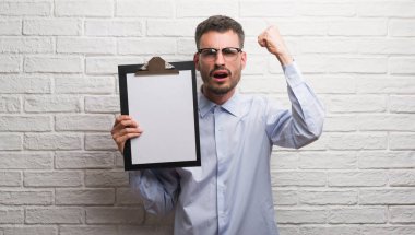 Genç Yetişkin iş adamı üzerinde tuğla duvar holding Pano rahatsız ve boşa çıkarmak ile öfke, çılgın ve yükseltilmiş eliyle diye bağıran öfke kavramı bağırarak.