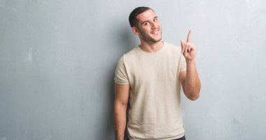 Gri grunge duvar bir fikir ya da soru işaret parmağı ile gülen yüz, sürpriz genç beyaz adam bir numara