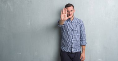 Beyaz delikanlı dur yapıyor gri grunge duvarın üzerinden elin avuç ile şarkı. Negatif ve ciddi bir jest yüz ifadesiyle uyarı.