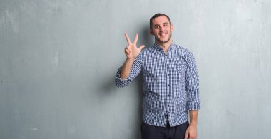 Beyaz delikanlı gösterilen ve parmakları ile işaret gri grunge duvarın üzerinden üçüncü ise kendinden emin ve mutlu gülümseyerek.